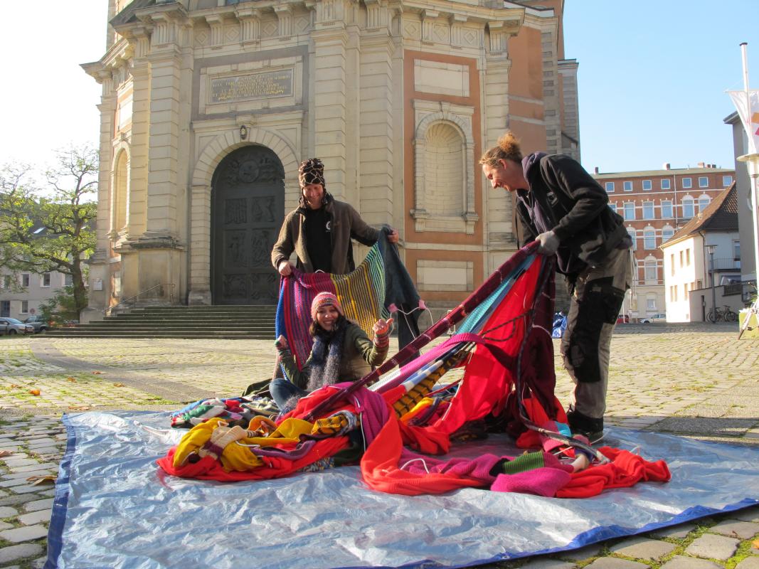 Die Künstlerin Mansha Friedrich nahm Teile des Strickgraffitis am Boden von den Industriekletterern Thomas Krohn (l.) und Ralph Eimann im Empfang. Aufgearbeitet zu Decken und Schals sollen diese im Dezember zugunsten der Ökumenischen Essensausgabe versteigert werden. © pkh